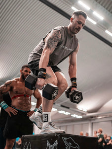A photo showing a guy wearing a faded sleeveless t-shirt.  The shirt has the famous ‘The Defiant Co’ logo across the front of the chest.  The sleeveless has a round neck and is slightly oversized.  The sleeveless is faded grey.  The guy is performing dummbbell box step overs during a crossfit workout.