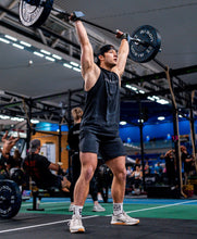 Load image into Gallery viewer, A photo showing a guy wearing a faded sleeveless t-shirt.  The shirt has the famous ‘The Defiant Co’ logo across the front of the chest.  The sleeveless has a round neck and is slightly oversized.  The sleeveless is faded black.  The guy is performing shoulder to overhead with 60kg during a crossfit workout.