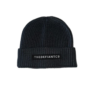 A photo showing a beanie hat. The hat has a ribbed finish with a roll cuff.  The cuff has The Defiant Co logo embroidered on the centre of the front in white on a black background. The beanie hat is charcoal.