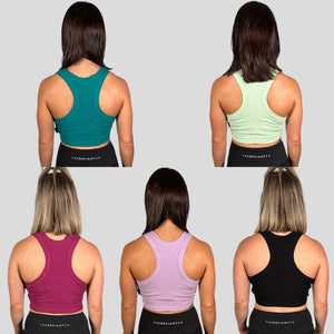 A photo collage of two girls wearing the 5 colours available in the DFNT. ribbed cropped tank - Black, Orchid Flower, Lime, Teal & Lilac.  The tanks have a high neck and are naturally breathable.  The fabric is soft to the touch and stretchy. The logo placement is via a tag sewn into the left seam.