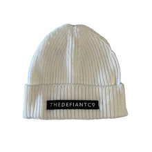 Load image into Gallery viewer, A photo showing a beanie hat. The hat has a ribbed finish with a roll cuff.  The cuff has The Defiant Co logo embroidered on the centre of the front in white on a black background. The beanie hat is white.