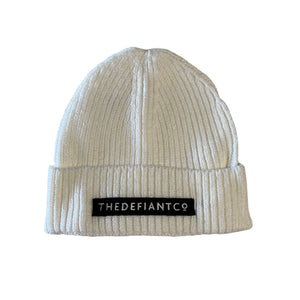 A photo showing a beanie hat. The hat has a ribbed finish with a roll cuff.  The cuff has The Defiant Co logo embroidered on the centre of the front in white on a black background. The beanie hat is white.