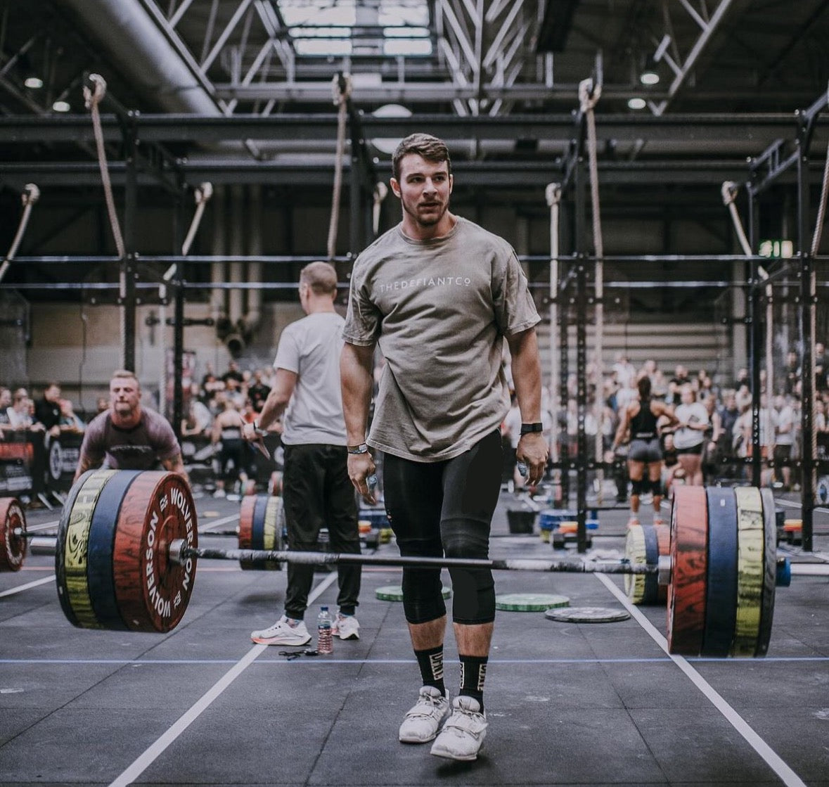 A photo showing a guy wearing an oversized The Defiant Co T-Shirt.  The shirt has the famous ‘The Defiant Co’ logo across the front of the chest.  The shirt has a round neck and is oversized.  This particular version has a washed finish and is the colour Asphalt.