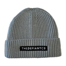 Load image into Gallery viewer, A photo showing a beanie hat. The hat has a ribbed finish with a roll cuff.  The cuff has The Defiant Co logo embroidered on the centre of the front in white on a black background. The beanie hat is light grey.