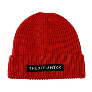 A photo showing a beanie hat. The hat has a ribbed finish with a roll cuff.  The cuff has The Defiant Co logo embroidered on the centre of the front in white on a black background. The beanie hat is red.