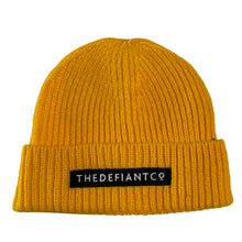 Load image into Gallery viewer, A photo showing a beanie hat. The hat has a ribbed finish with a roll cuff.  The cuff has The Defiant Co logo embroidered on the centre of the front in white on a black background. The beanie hat is mustard.