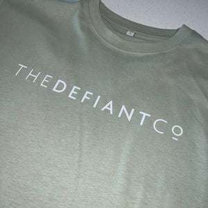 A photo showing an oversized The Defiant Co T-Shirt.  The shirt has the famous ‘The Defiant Co’ logo across the front of the chest.  The shirt has a round neck and is oversized.  This particular version is the colour sage green.