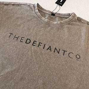 A photo showing an oversized The Defiant Co T-Shirt.  The shirt has the famous ‘The Defiant Co’ logo across the front of the chest.  The shirt has a round neck and is oversized.  This particular version has a washed finish and is the colour khaki.