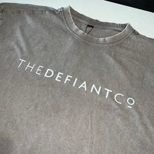 Load image into Gallery viewer, A photo showing an oversized The Defiant Co T-Shirt.  The shirt has the famous ‘The Defiant Co’ logo across the front of the chest.  The shirt has a round neck and is oversized.  This particular version has a washed finish and is the colour asphalt with white print.