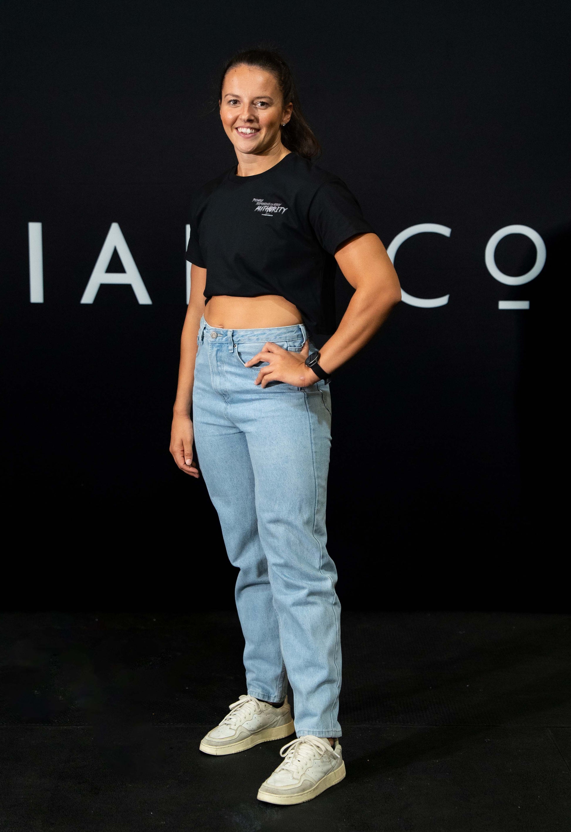 A girl against a black The Defiant Co backdrop wearing the proudly refusing to obey authority cropped t-shirt in black with jeans and trainers.