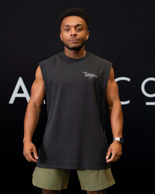 A guy against a black The Defiant Co backdrop wearing the proudly refusing to obey authority sleeveless tee, olive green performance shorts.