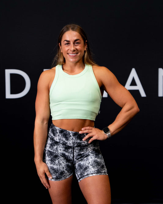 A girl against a black The Defiant Co backdrop wearing the DFNT. Ribbed Cropped Tank.  The tank is breathable with a stretchy fabric so is perfect for working out in.  It has a subtle DFNT. logo on a tag.  The colour is lime.