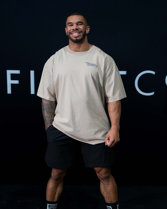 A guy against a black The Defiant Co backdrop wearing the faded khaki proudly refusing to obey authority oversized tee and black performance shorts. 