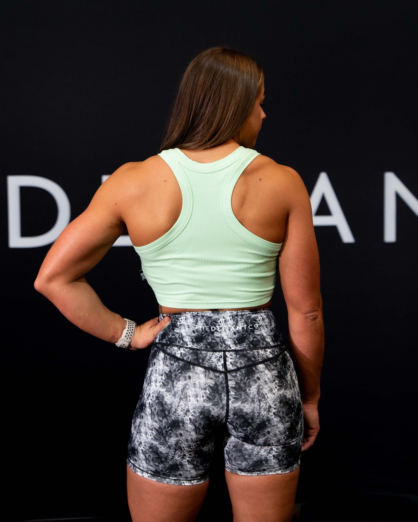 A girl against a black The Defiant Co backdrop wearing the DFNT. Ribbed Cropped Tank.  The tank is breathable with a stretchy fabric so is perfect for working out in.  It has a subtle DFNT. logo on a tag.  The colour is lime.