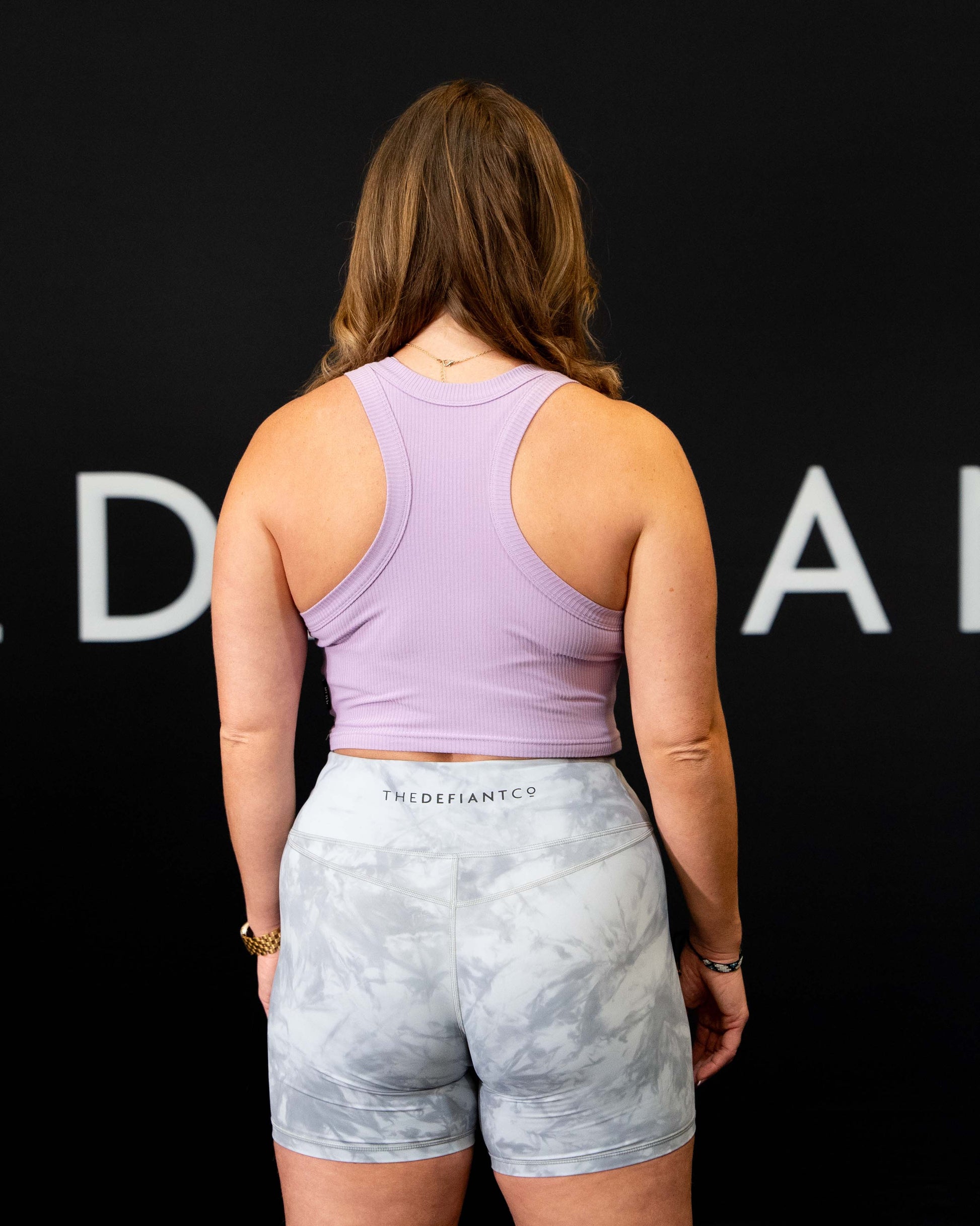 A girl against a black The Defiant Co backdrop wearing the DFNT. Ribbed Cropped Tank.  The tank is breathable with a stretchy fabric so is perfect for working out in.  It has a subtle DFNT. logo on a tag.  The colour is lilac.