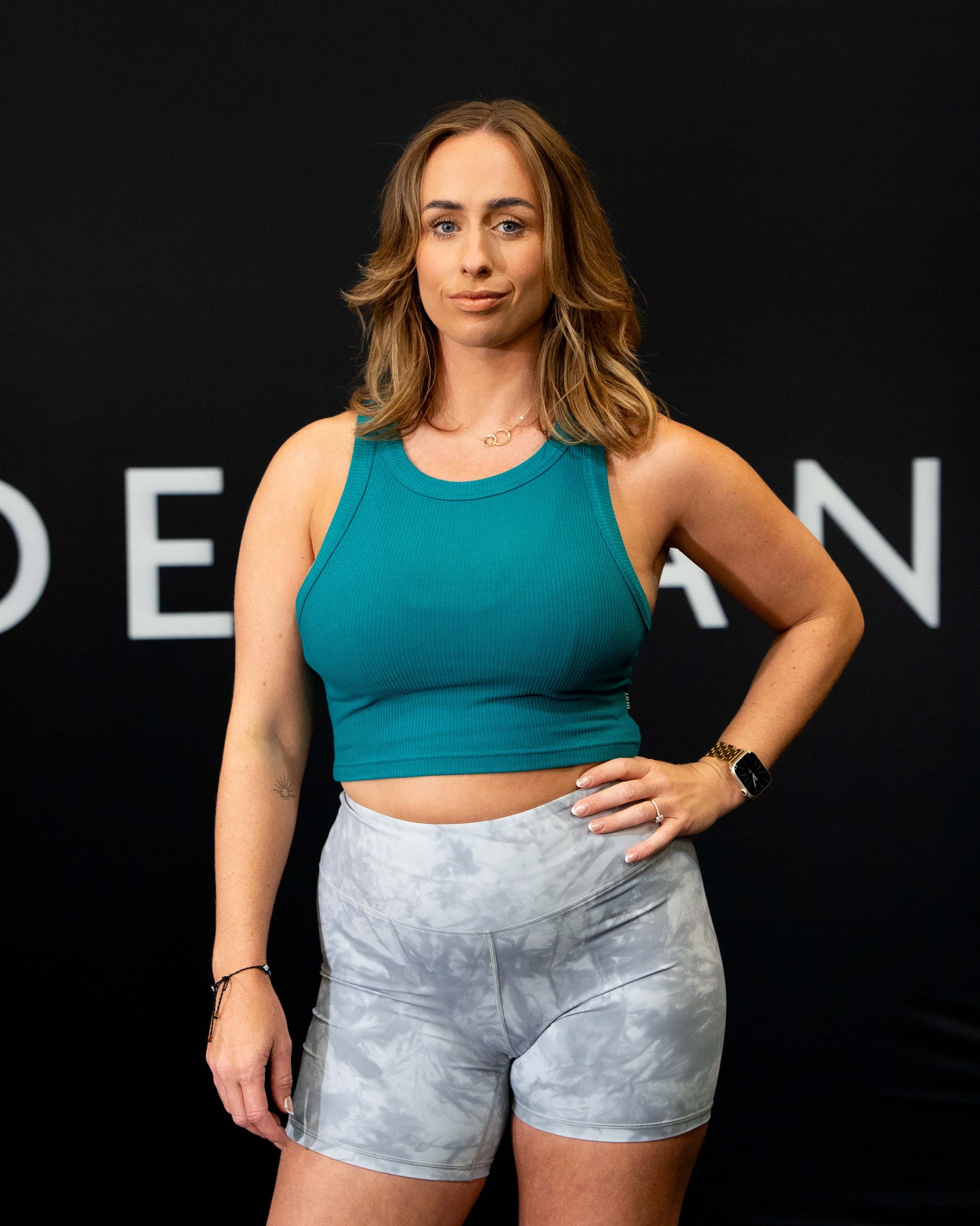 A girl against a black The Defiant Co backdrop wearing the DFNT. Ribbed Cropped Tank.  The tank is breathable with a stretchy fabric so is perfect for working out in.  It has a subtle DFNT. logo on a tag.  The colour is teal.