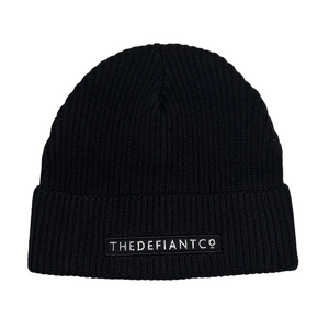 A photo showing a beanie hat. The hat has a ribbed finish with a roll cuff.  The cuff has The Defiant Co logo embroidered on the centre of the front in white on a black background. The beanie hat is black.
