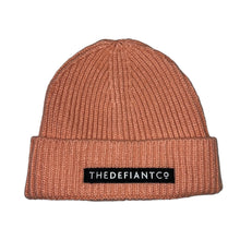 Load image into Gallery viewer, A photo showing a beanie hat. The hat has a ribbed finish with a roll cuff.  The cuff has The Defiant Co logo embroidered on the centre of the front in white on a black background. The beanie hat is salmon.