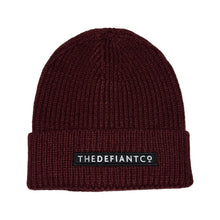 Load image into Gallery viewer, A photo showing a beanie hat. The hat has a ribbed finish with a roll cuff.  The cuff has The Defiant Co logo embroidered on the centre of the front in white on a black background. The beanie hat is burgundy.